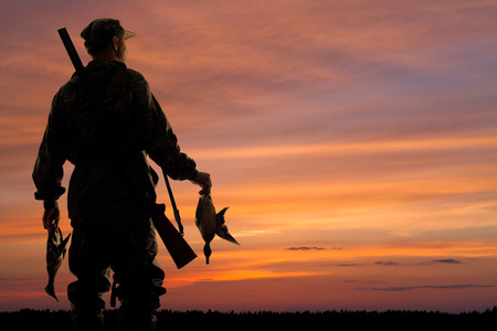 silhouette of the duck hunter with prey on the sunset backgroundの写真素材