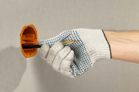 electrician's hand in a glove pulls the cable into the box sockets on the drywall wall, closeupの写真素材