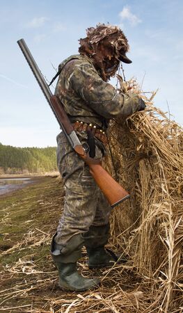 duck hunter with a shotgun is preparing a place to hunt on the shoreの写真素材