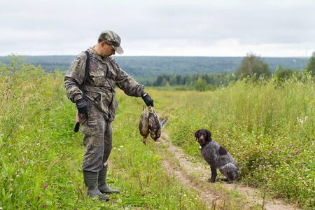 hunter with his gundog is on the field road with prey in hand