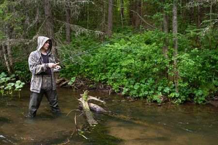 a fisherman with a spinning rod in his hands stands in shallow water on a little northern riverの写真素材