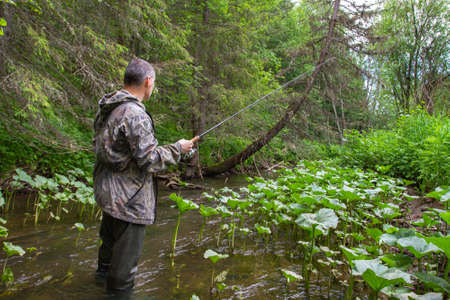 a fisherman with a spinning rod is fishing in a small forest river in the Northの写真素材