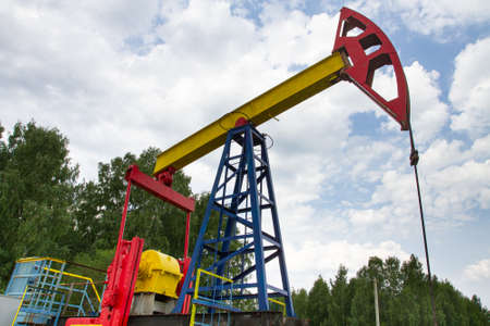 oil pumpjack against a cloudy sky stands among the treesの写真素材