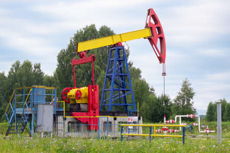 a lone oil pumpjack stands among the trees in an oil fieldの写真素材