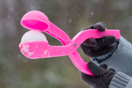hands of a woman dressed in gloves hold the plastic form for making a snowballの写真素材