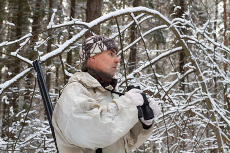 a huntsman dressed in white camouflage with binoculars in his hands is in the snowy northern forestの写真素材
