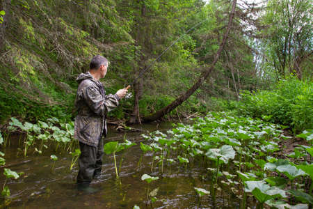 fisherman with a spin fishing rod in his hands stands in the middle of a narrow forest riverの写真素材