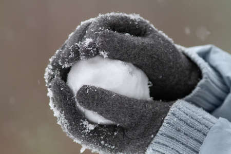 gloved hands mold a snowball out of fresh snowの写真素材