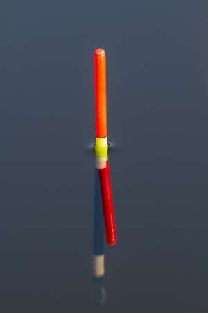 the orange tip of the fishing float sits vertically in blue water of the lake, close upの写真素材