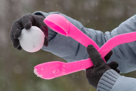 hands of a woman dressed in gloves hold the pink plastic form for making a snowballの写真素材