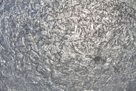 The uneven patterned surface of transparent ice, through which the sun shines through. Abstract winter background for Christmas and New Year.の写真素材