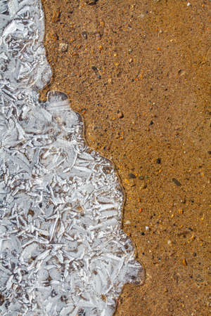 The shoreline of the reservoir on a frosty day. Openwork patterned ice and red sand in the water. Close-up.の写真素材