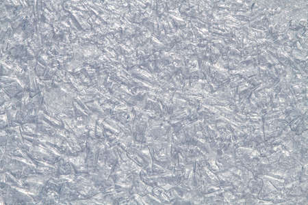 Smoothed patterned surface of ice formed by small rounded pieces of ice and spots of frozen water. Through it shines the light of day. Abstract winter background for Christmas and New Year.の写真素材