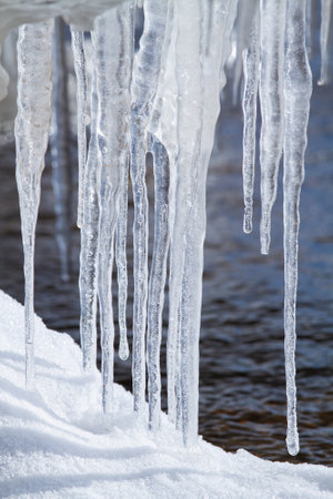 A few icicles grew on the snow-covered riverbank during the thaw.の写真素材