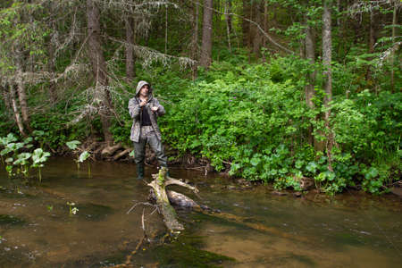 a fisherman with a spinning rod in his hands catches fish on the bank of a small northern river, which is overgrown with forestの写真素材
