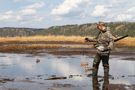 Waterfowler with a duck decoy in his hand is on the muddy shallow water. He's getting ready for a duck hunt.の写真素材