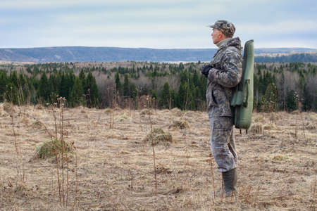 A shotgun case is slung over the shoulder of a hunter standing in a clearing.