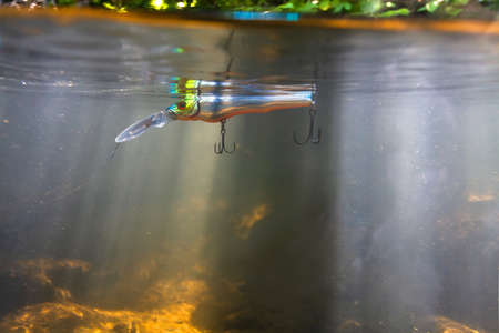 Fishing with spinning. On the surface of the river water, covered with ripples, a silver wobbler floats attached to a fishing line. The sun's rays penetrate the water column. A look from under the water. Close-up.の写真素材