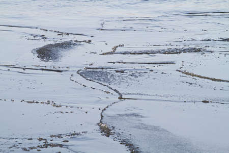 The thin ice sheet split into separate ice floes. Water is visible in the cracks. The surface of the ice floes is wet and covered with water.の写真素材