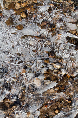 On a frosty winter day, the water level dropped, exposing the shoal. Transparent openwork ice covers the coastal pebbles with sand. Close-up.の写真素材