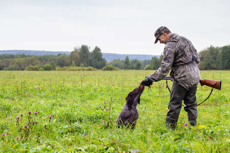 a hunter holds a downed crake in his hand, which was brought by his dog (German wire-haired pointer) during the hunt.の写真素材