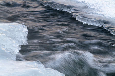 A fast river stream flows between the ice floes. Foam is visible on its surface.の写真素材
