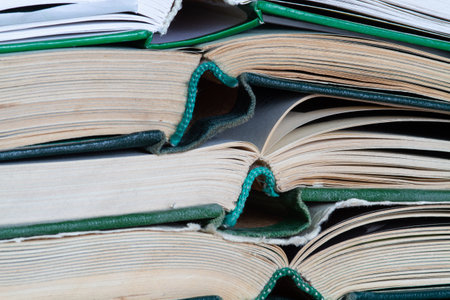 Several large books lie on top of each other, forming a stack. You can see their worn bindings. close-up.の写真素材