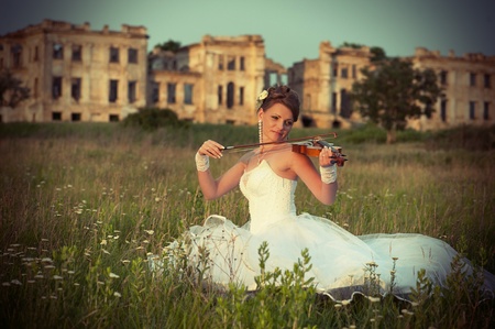 Bride with violin sitting on the grass in front of ruins at sunsetの写真素材