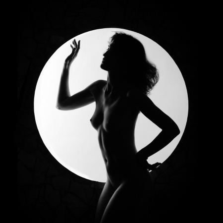 Black silhouette of nude woman in light circle on dark backgroundの写真素材