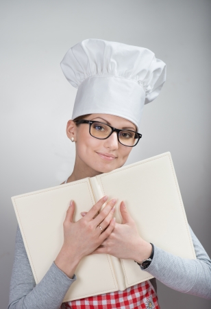 Closeup portrait of smiling woman in chef s hat with the book on grey backgroundの写真素材