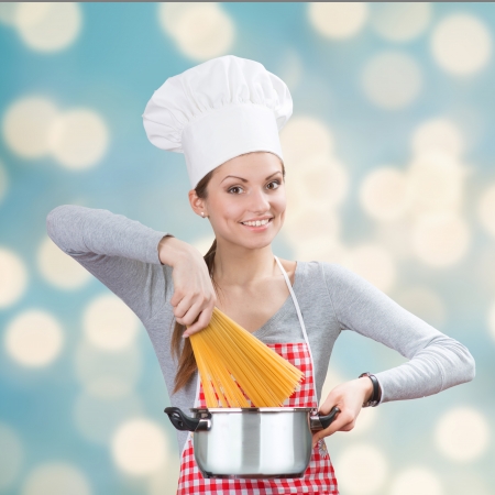 Portrait of a smiling woman in chef s hat adding the pasta to the pot on the blue abstract backgroundの写真素材