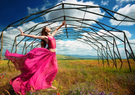 Outdoors portrait of a woman in airy crimson dress in front of the old metallic construction in windy spring dayの写真素材