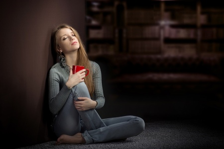 Young woman with red cup sitting on the floor and dreamingの写真素材