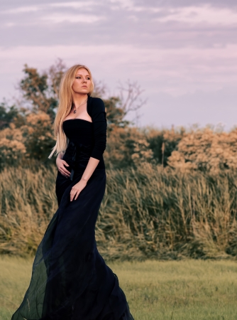 Outdoors portrait of a blond woman in long black dress at sunsetの写真素材