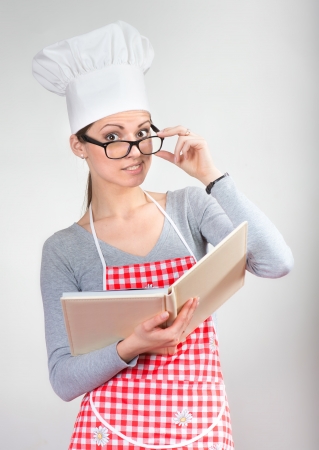 Funny portrait of a woman in chef s hat with the cookbook looking over the glassesの写真素材