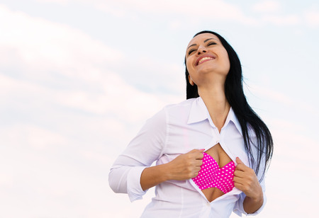 Smiling business lady unbuttoning her white shirt and revealing a pink bikini, outdoors portrait