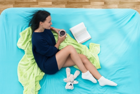 Pretty girl drinking coffee and reading a book in bedの写真素材