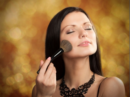 Close-up portrait of a pretty woman with cosmetic brush on abstract backgroundの写真素材