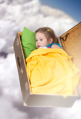 Dreaming little girl flying in the cloudy sky in an old suitcaseの写真素材