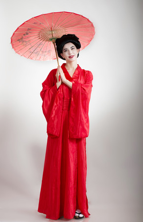 Asian style portrait of a woman in red kimono with umbrella, gray backgroundの写真素材