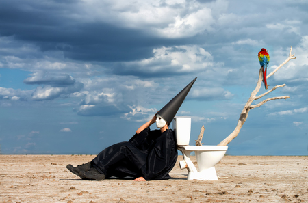 Strange person in black cloak sitting on the toilet and thinking in the middle of the desertの写真素材