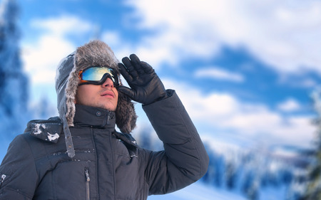 Winter holiday - portrait of a man wearing an ear flap hat and ski glasses with mountains in backgroundの写真素材