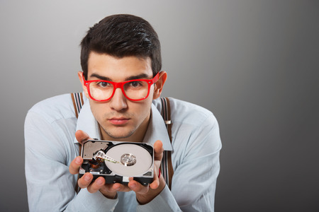 Man in red-framed glasses with hard disk drive in his hands looking at cameraの写真素材