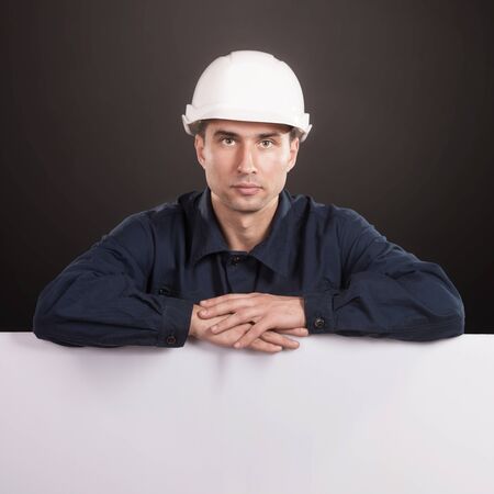 Portrait of a workman in dark blue coveralls and white hardhat looking at cameraの写真素材