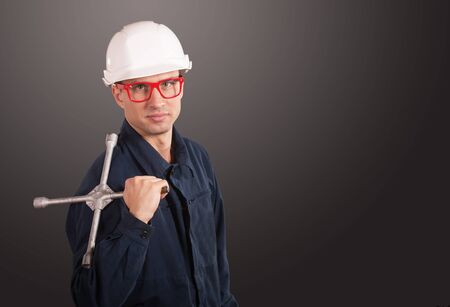 Portrait of a workman in dark blue coveralls and white hardhat with a wheel wrenchの写真素材