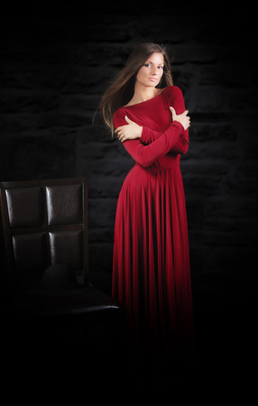 Woman in long red dress, studio portrait, dark backgroundの写真素材