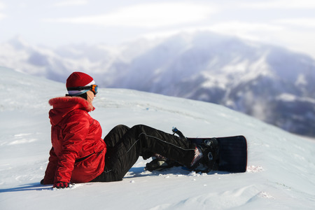 Woman with snowboard sitting in the snow, mountains in the backgroundの写真素材