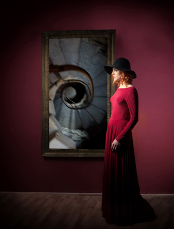 Woman's portrait against the picture with spiral stairs hanging on a wallの写真素材