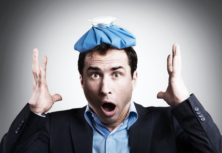 Shocked office worker with an ice pack on his head. Unpaid sick leave conceptの写真素材