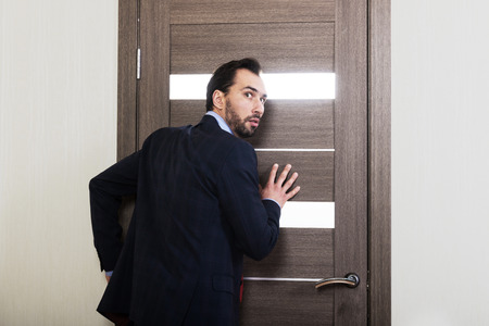 Eavesdropping at work. Inquisitive man listening through the office doorの写真素材